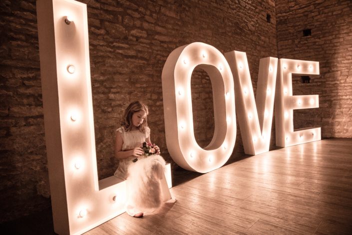 Bridesmaid sitting on illuminated Love signage
